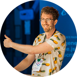 Josh smiling and giving a thumbs up at a podium wearing a white shirt with a pineapple pattern